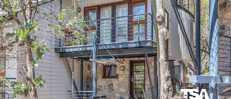 Een gebouw met twee verdiepingen, een gevel van natuursteen, een balkon met metalen hekwerk en een trap naar de ingang.