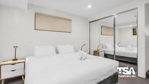 Ein modernes Hotelzimmer mit einem großen Bett, Nachttischen, einem Spiegel und einer Schiebetür.