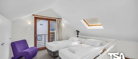 A hotel room with a bed, a purple chair, a window with curtains, and a skylight.