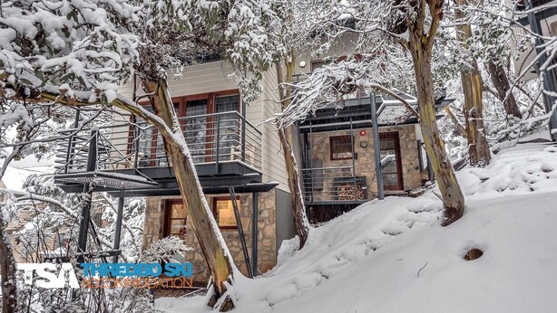 Ein mit Schnee bedecktes Gebäude mit einer Stein-Fassade, einer Metalltreppe und einem Holzbalkon.
