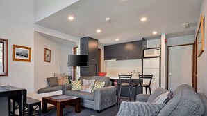 A modern living room with a sofa, a coffee table, a TV, and a kitchen area with a microwave and cabinets.