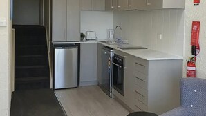 A compact kitchen with a refrigerator, oven, and toaster. There is a small seating area with a chair.