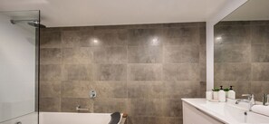 Bathroom features a large mirror, wall-mounted faucet, and a glass-enclosed tub with handheld showerhead.