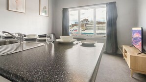 A modern kitchen with a granite countertop, stainless steel sink, and a window with a view of buildings and a pool. - Razorback 14 - Centrally located, lovely 1 bedroom (Jindabyne)