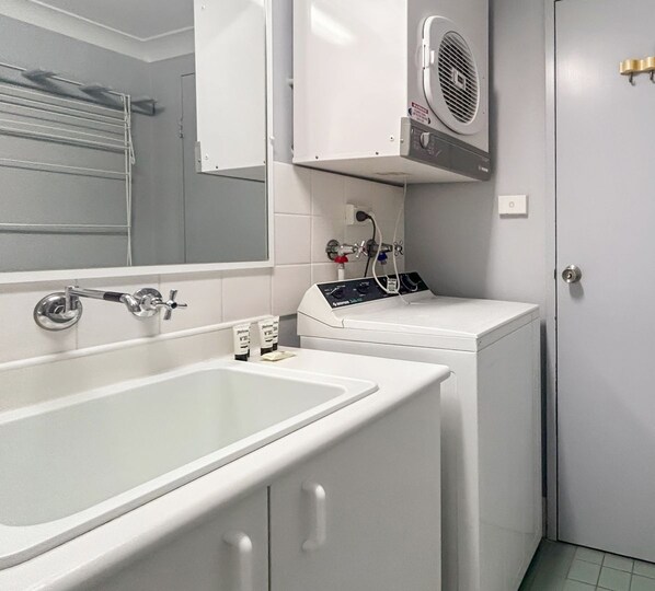 Une salle de bain avec un lavabo blanc, un lave-linge et un miroir.