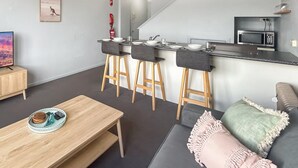 A compact living space with a TV, wooden furniture, a kitchen area, and a couch. - Razorback 14 - Centrally located, lovely 1 bedroom (Jindabyne)