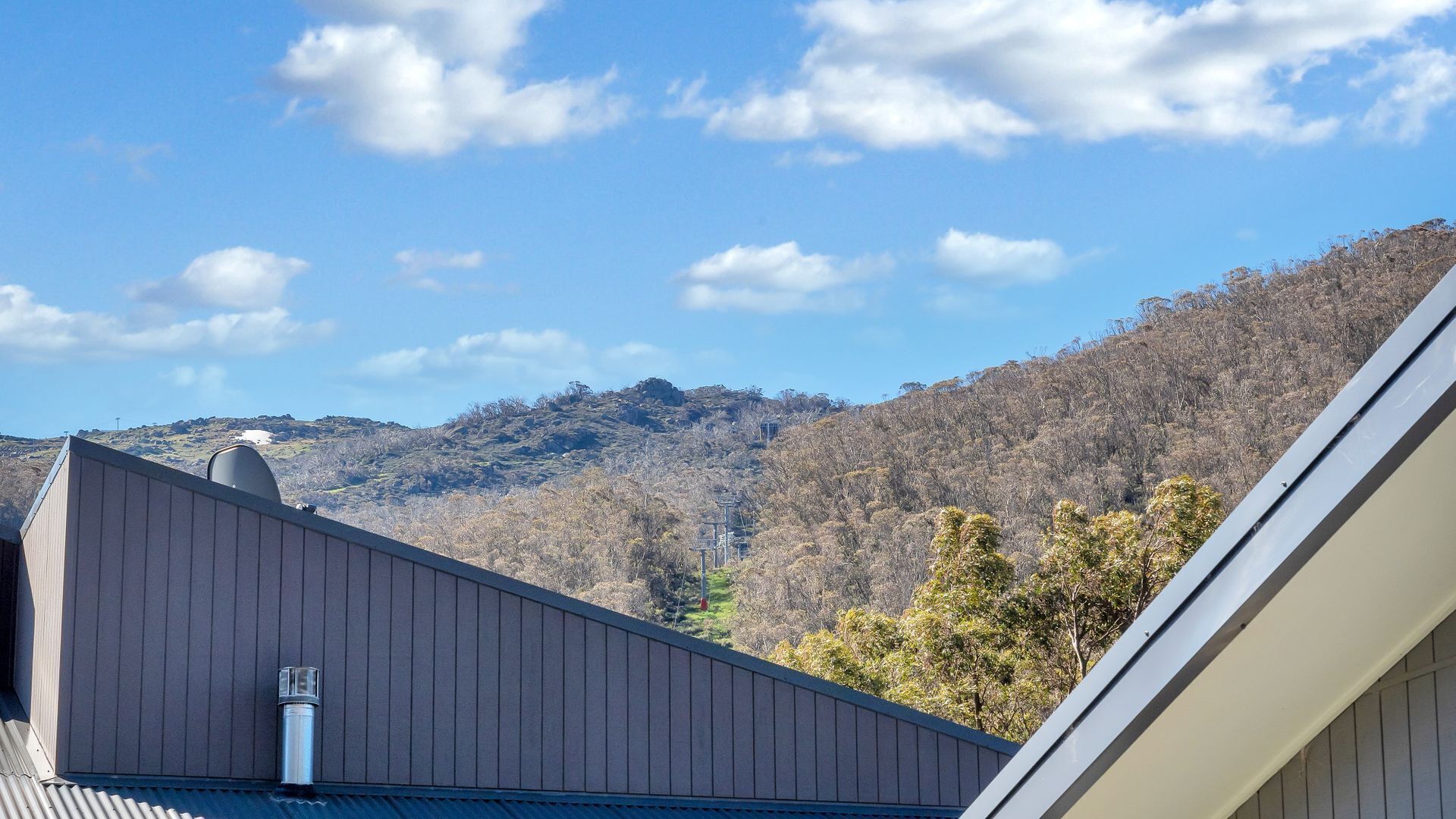 A building with a sloped roof, a chimney, and a view of a mountainous landscape under a clear sky.