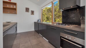 A modern kitchen with dark cabinetry, a large window, and a view of trees.