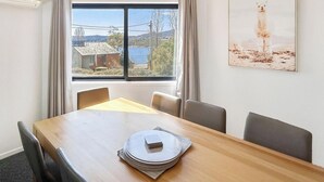 Un comedor con una mesa de madera, sillas y vistas a una casa y al paisaje a través de una ventana.