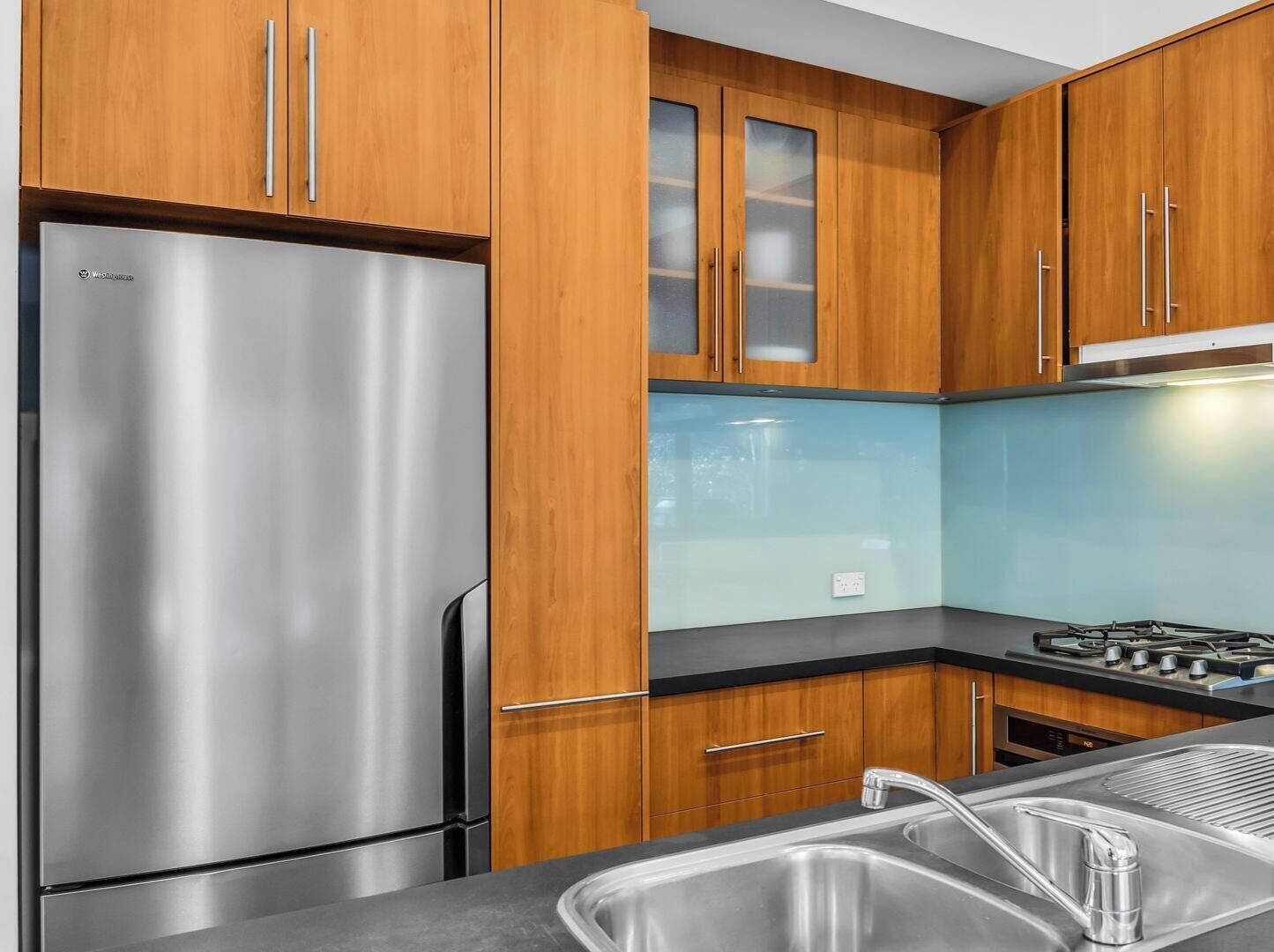 A kitchen with wooden cabinets, a stainless steel refrigerator, a gas stove, and a sink.