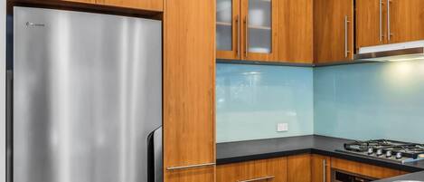 A kitchen with wooden cabinets, a stainless steel refrigerator, a gas stove, and a sink.