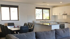 A modern kitchen with white cabinets, a central island, and a dining area with a gray sofa and chairs. - The Summit 15 - Spacious 4 bedroom with lake views (Jindabyne)