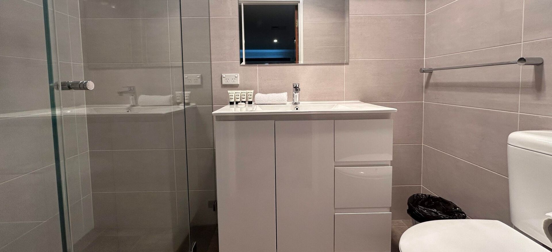A modern bathroom with a glass shower enclosure, a pedestal sink, and a toilet.