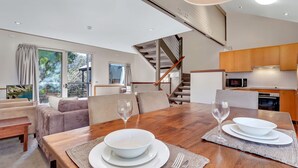 Una sala moderna con una mesa de comedor de madera dispuesta para dos personas, un sofá y una escalera que lleva a un nivel superior.