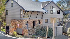 Una casa moderna de dos pisos con base de piedra, ventanas amplias y techo de metal.
