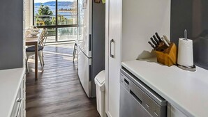 A kitchen with a view of a lake, a dining area with a table and chairs, and a white refrigerator. - The Summit 16 - Huge deck with lake views (Jindabyne)
