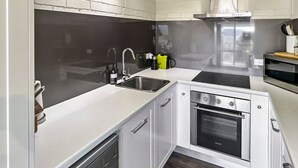 A compact kitchen with a built-in oven, a microwave, and a sink. - The Summit 16 - Huge deck with lake views (Jindabyne)