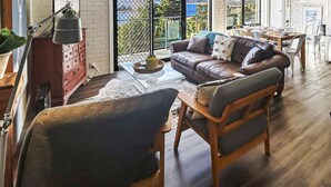 A cozy living room with a leather sofa, a wooden coffee table, and a dining area with a table and chairs. - The Summit 16 - Huge deck with lake views (Jindabyne)