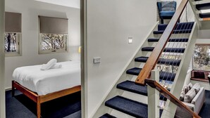 Een slaapkamer met een bed, een raam met uitzicht, een trap met blauwe treden en een houten leuning.