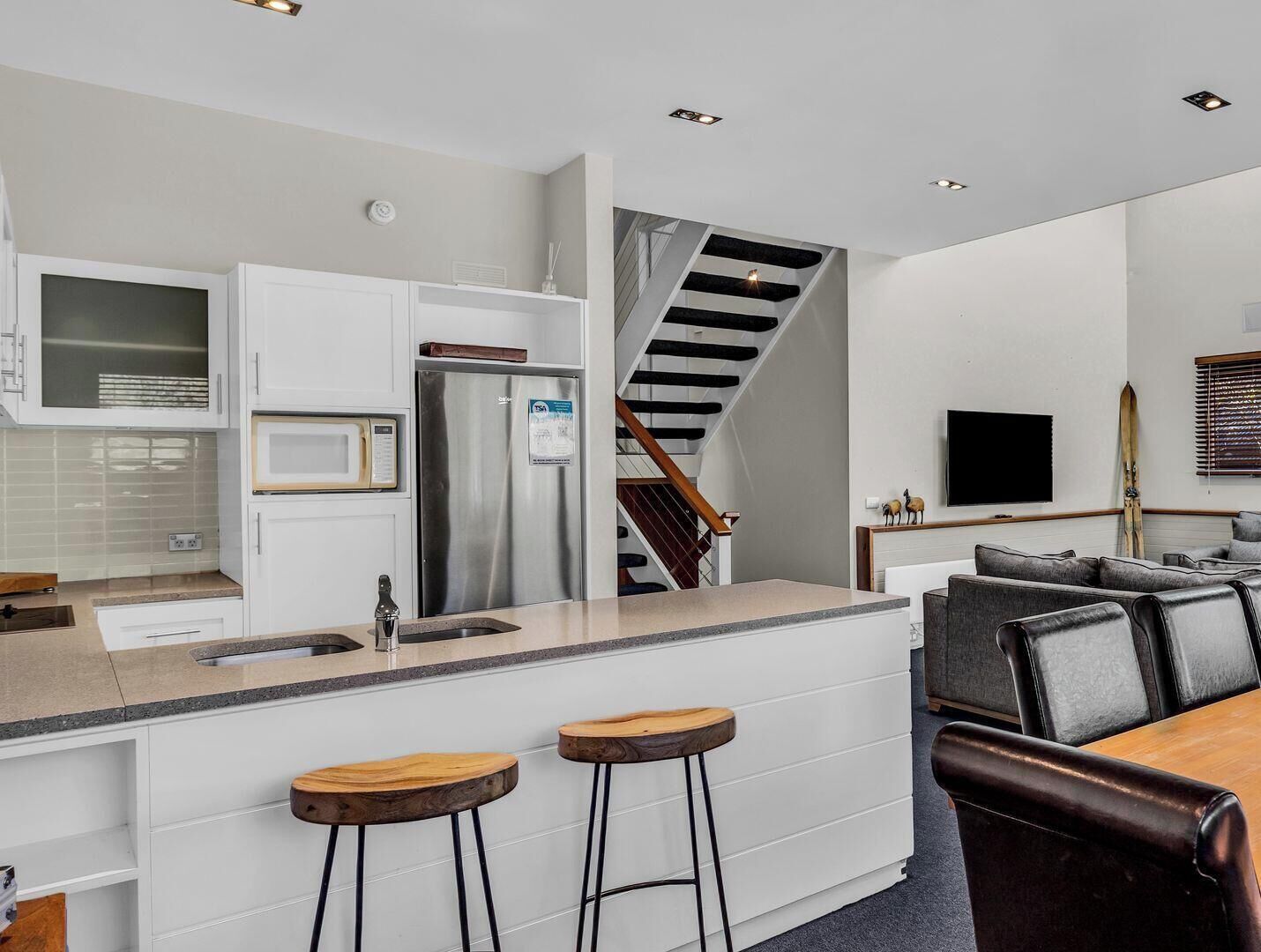 A modern kitchen with a stainless steel refrigerator, a microwave, and a wooden island with stools.