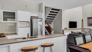 A modern kitchen with a stainless steel refrigerator, a microwave, and a wooden island with stools.