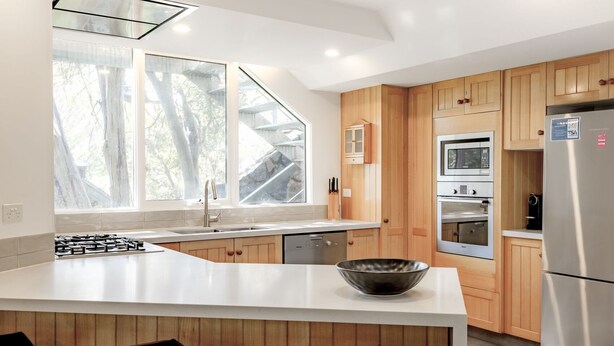 A modern kitchen with wooden cabinets, a stainless steel refrigerator, and a large window providing natural light. - Rileys Run - Woodridge (Woodridge)