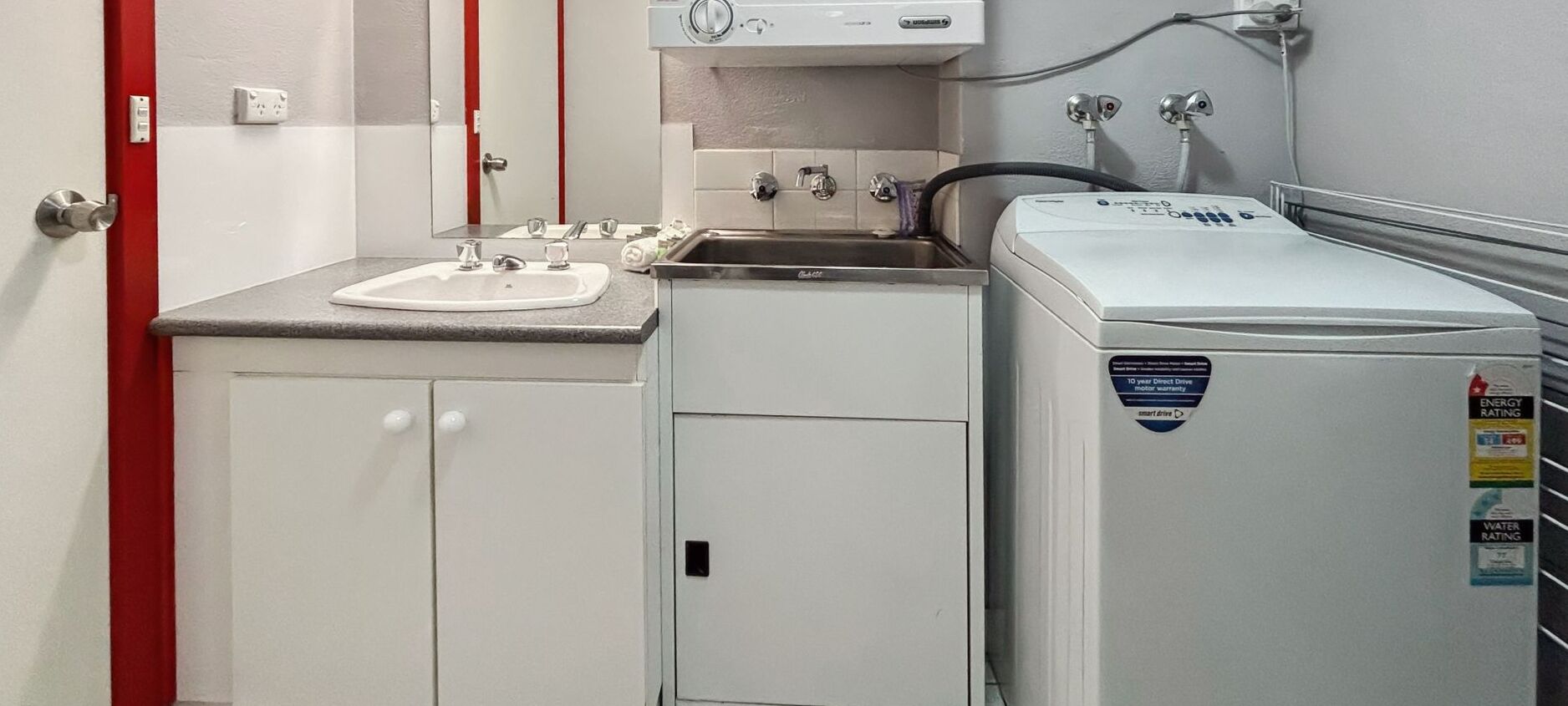 A compact hotel bathroom with a sink, mirror, and a washing machine.
