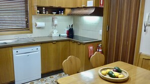 A compact kitchen with wooden cabinets, a dishwasher, a sink, and a table with a fruit bowl.