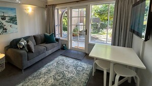 Un salon chaleureux avec un canapé gris, une petite table d’appoint avec une lampe, une table blanche et un tapis à motifs.