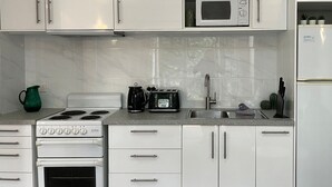 Une cuisine moderne avec des armoires blanches, un four à micro-ondes encastré, une cuisinière et un réfrigérateur.