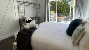 Une chambre à coucher avec un lit, une fenêtre avec des rideaux, une étagère en métal avec des serviettes et une vue sur l’extérieur.