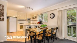 Una cocina moderna con armarios blancos, una isla central y un comedor con mesa y sillas de vidrio.