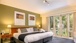 Habitación de hotel con cama, mesitas de noche, escritorio, silla y un amplio ventanal corredero que da a un área exterior.