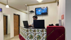 A reception area with a desk, two laptops, a television, and a red couch. - HOTEL WEST INN BOULEVARD (Srinagar)