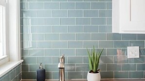A kitchen with white cabinets, a stainless steel sink, and a blue tiled backsplash. - Cute Boston Condo | Near T (Boston)