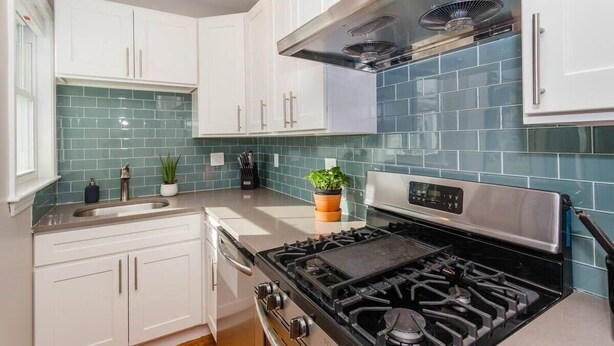 A kitchen with white cabinets, a stainless steel stove, and a blue-tiled backsplash. - Cute Boston Condo | Near T (Boston)