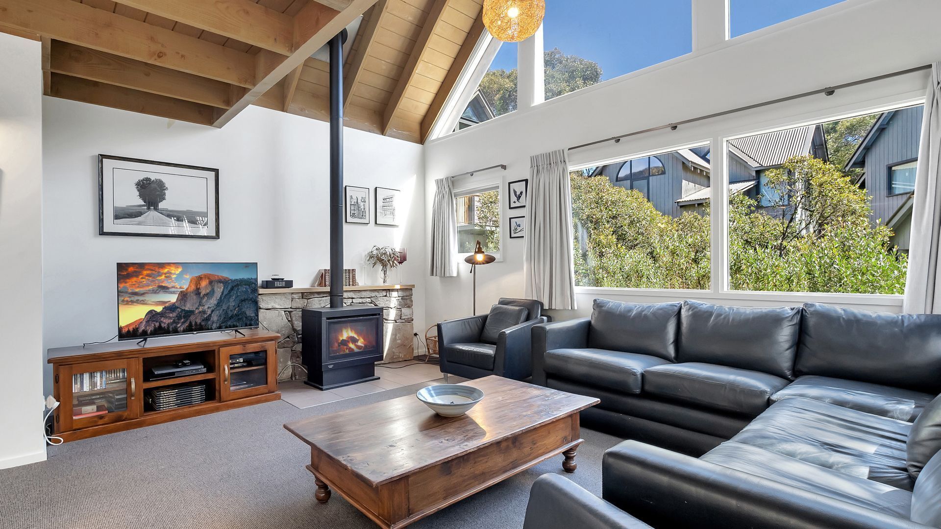 A modern living room with a stone fireplace, leather sofa, and a television on a wooden cabinet.