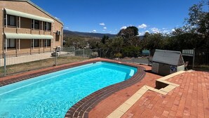 A rectangular swimming pool with a brick border, surrounded by a brick patio. - Alpine Mountain View 40 (Jindabyne)
