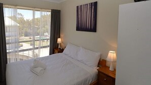 A hotel room with a bed, two bedside lamps, a window with curtains, and a painting on the wall. - Alpine Mountain View 40 (Jindabyne)