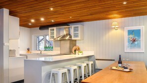 Uma cozinha moderna com armários brancos, teto de madeira e um espaço de refeições com mesa e banquetas.