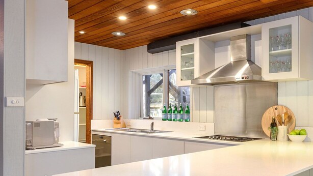 Uma cozinha moderna com armários brancos, exaustor de aço inoxidável, lava-louças embutida e uma janela que proporciona luz natural.