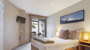 A bedroom with a bed, a nightstand with a lamp, a TV mounted on the wall, and a painting above the bed.