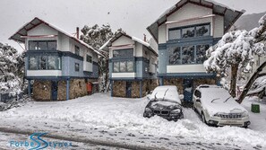 Una casa de dos pisos con garaje, rodeada de árboles cubiertos de nieve.