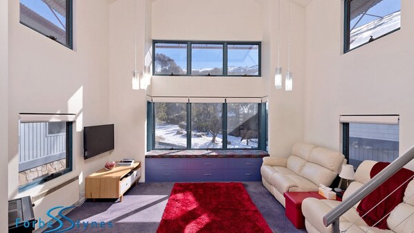 Una sala de estar moderna con un ventanal grande, un sofá, una alfombra roja y un televisor.
