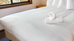 Een keurig opgemaakt bed met witte lakens en een opgevouwen handdoek.
