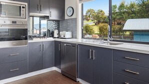 Eine moderne Küche mit grauen Schränken, einem Backofen, einer Mikrowelle und einem Geschirrspüler. Ein Fenster bietet einen Blick ins Freie.