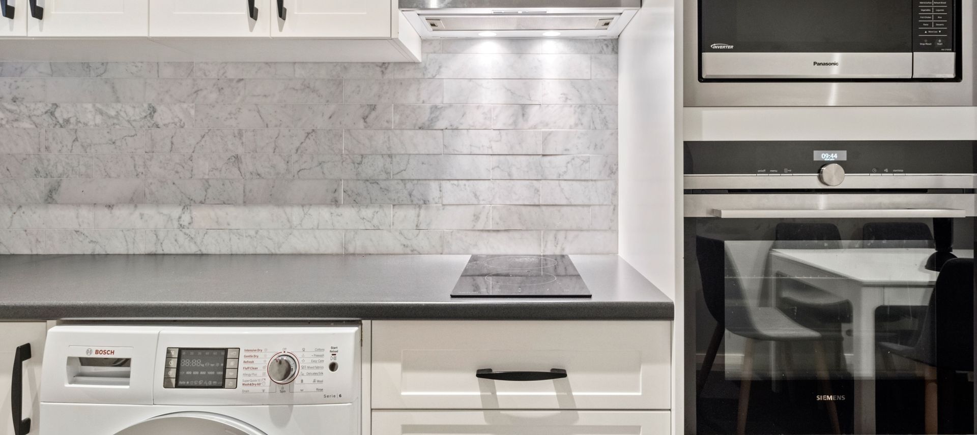 Uma cozinha equipada com máquina de lavar Bosch, micro-ondas Siemens e forno Panasonic.
