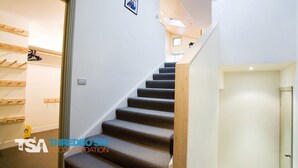 Eine Treppe mit Teppichstufen führt zu einer Zwischenebene, eine Holzwand mit Haken und eine weiße Tür.