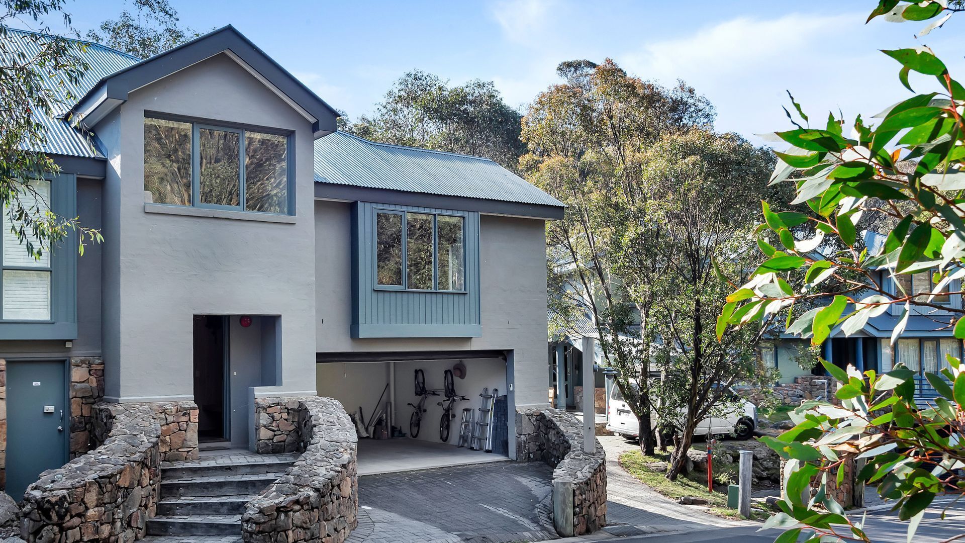 A two-story house with a stone staircase leading to the front door, a garage with bicycles, and a driveway.