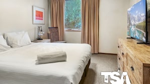 A hotel room with a large bed, a TV on a wooden cabinet, a window with curtains, and a framed picture on the wall.